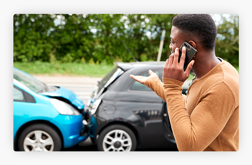Man Talking on the Phone While a Car is Crashed Behind Him