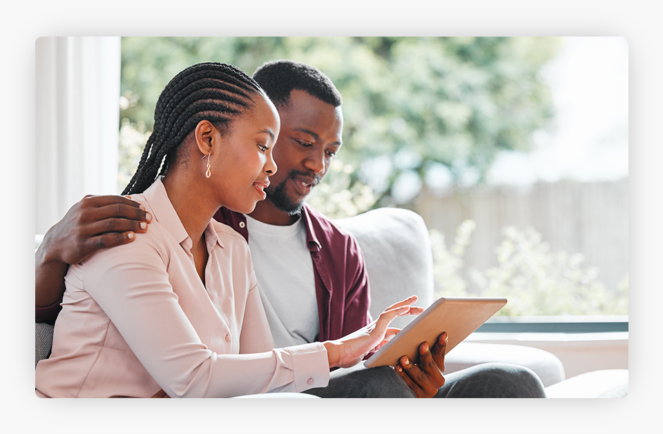 A young couple smiling as they check a tablet on a cozy sofa.