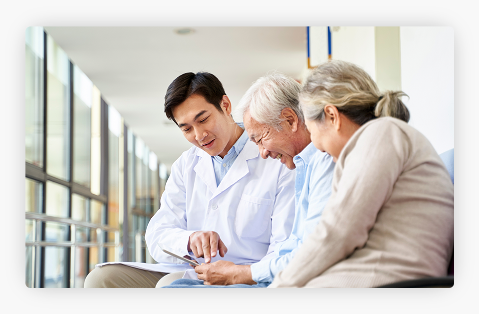 A young Asian doctor discussing test results and a diagnosis with an elderly couple of patients.