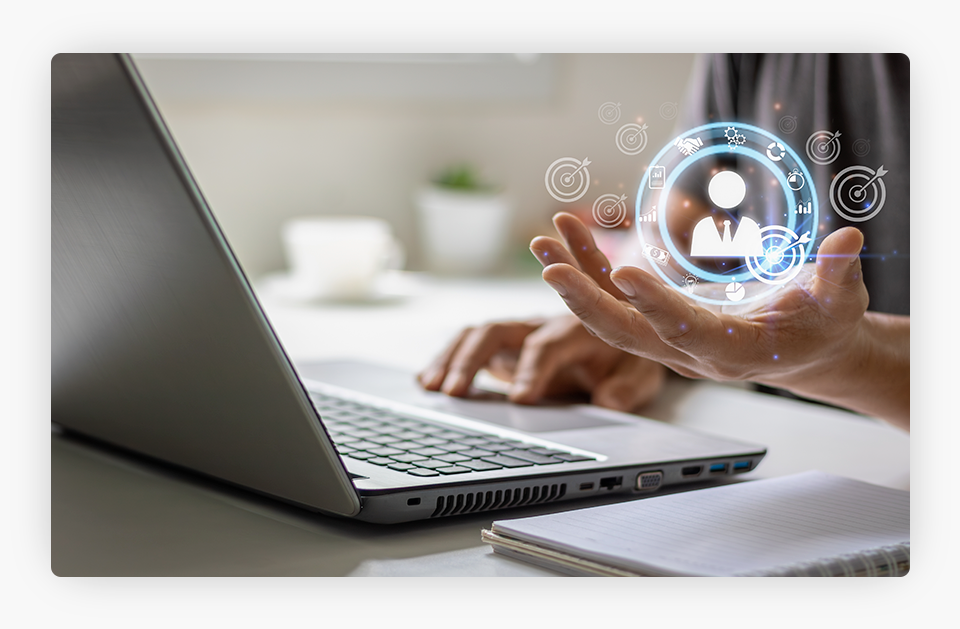 A man on a laptop, holding a floating digital icon with his left hand.